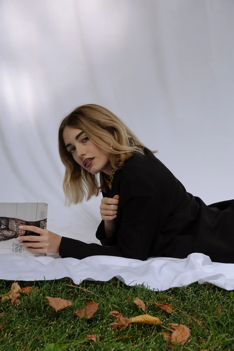 Bianco Silenzio: Alessia sdraiata sul lenzuolo nel prato tra le foglie secche, con una rivista