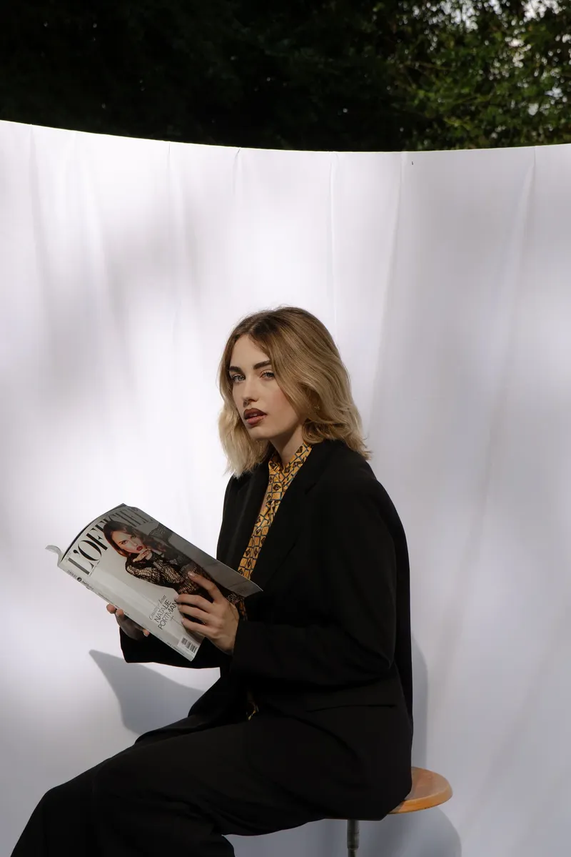 Bianco Silenzio: Alessia seduta su uno sgabello sfoglia una rivista davanti al lenzuolo bianco