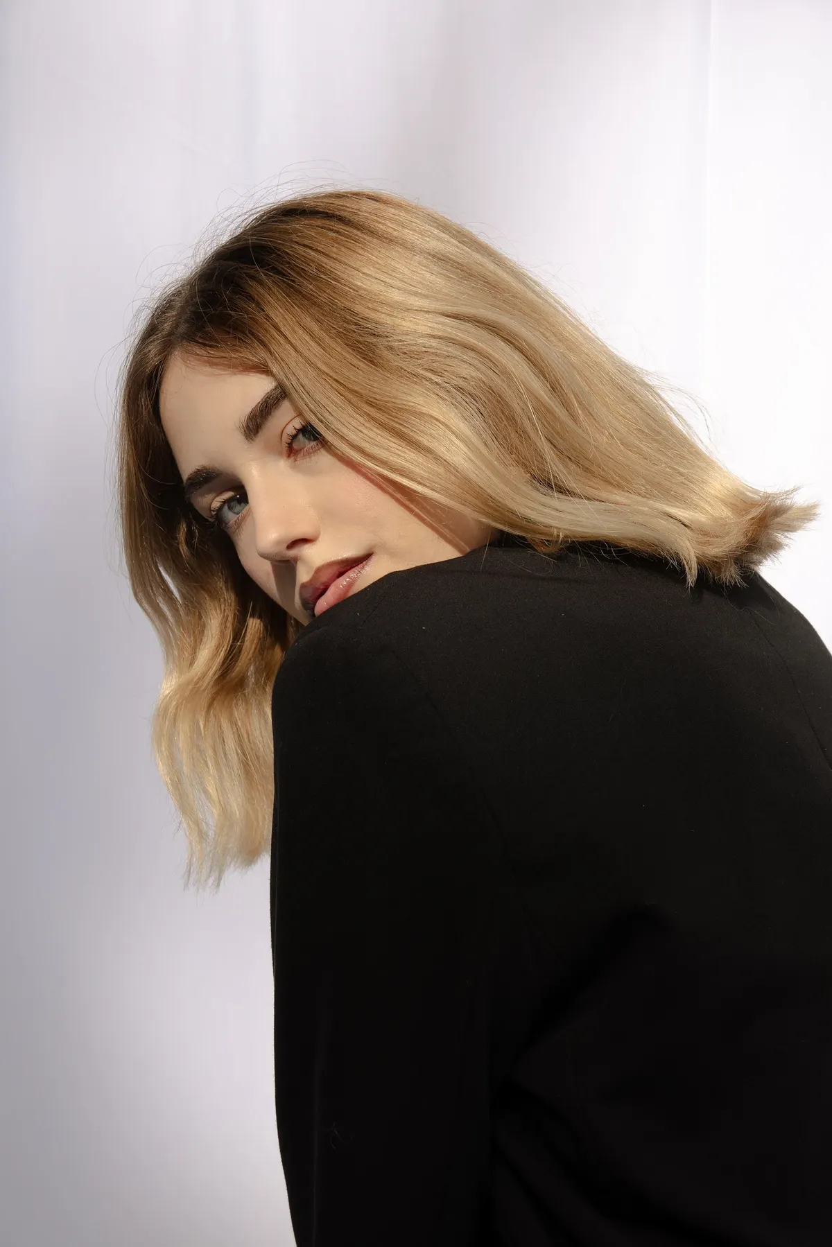 Bianco Silenzio: Alessia in blazer nero si volta verso l’obiettivo davanti al lenzuolo bianco