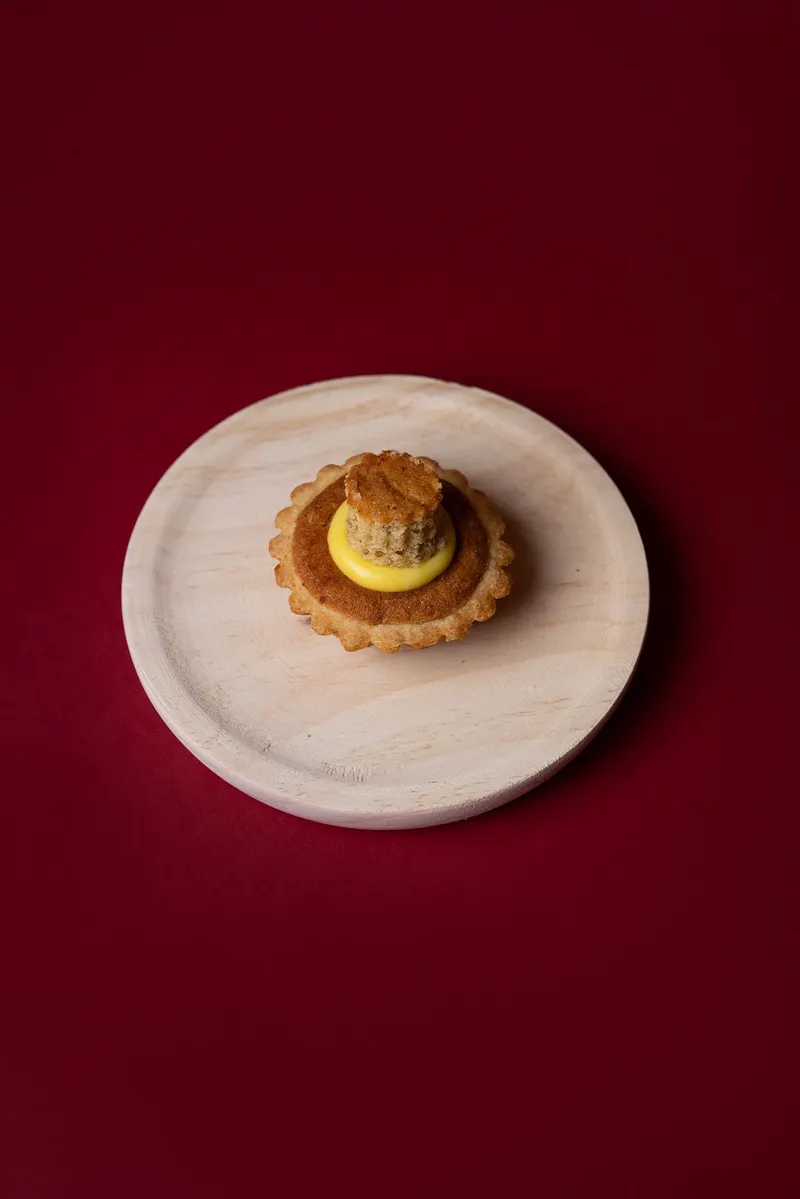 Tortina con crema gialla vista dall’alto su tagliere tondo, fondale bordeaux