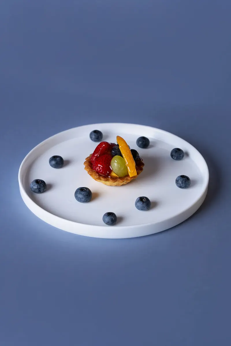 Crostatina alla frutta su piatto bianco con mirtilli, fondale blu
