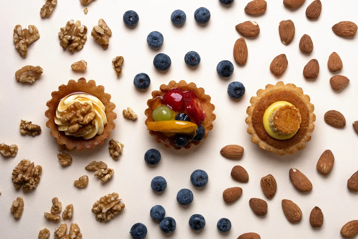 Tre pasticcini tra noci, mandorle e mirtilli su fondo chiaro