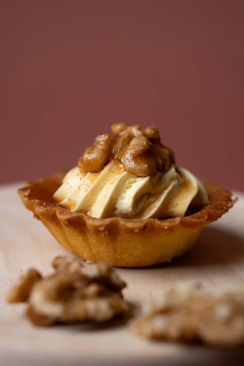 Pasticcino con crema e noci caramellate, noci sullo sfondo