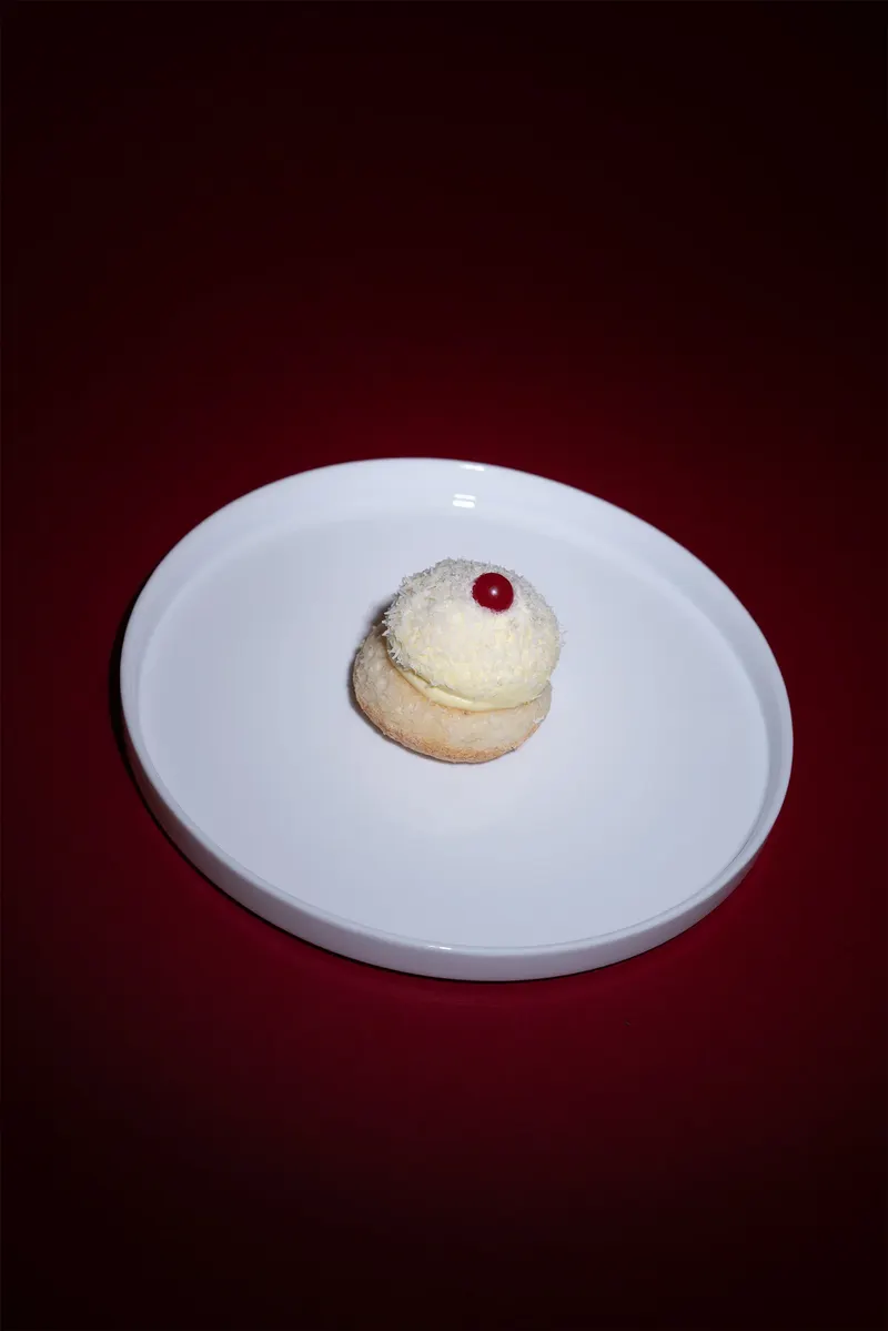 Pasticcino bianco con ribes su piatto, visto dall’alto su fondale scuro