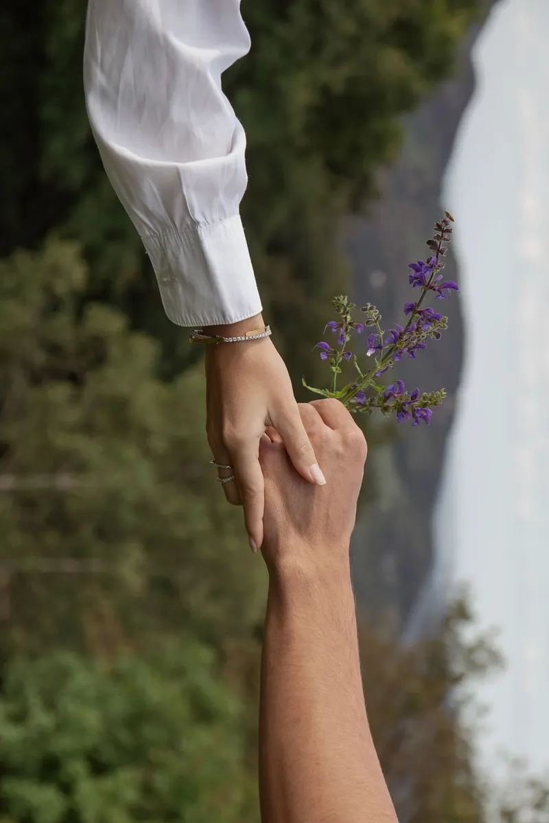 Dettaglio delle mani intrecciate con un rametto di fiori viola
