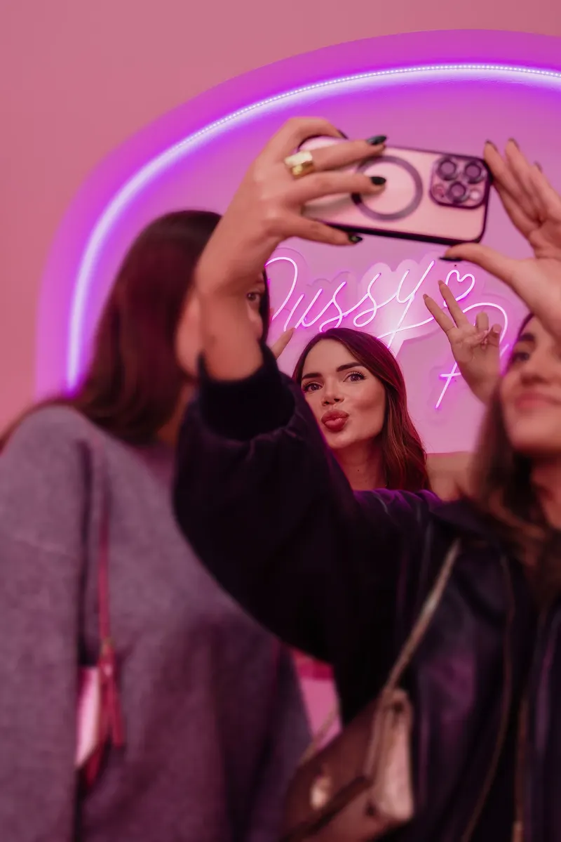 Ragazze scattano un selfie davanti all’insegna al neon rosa